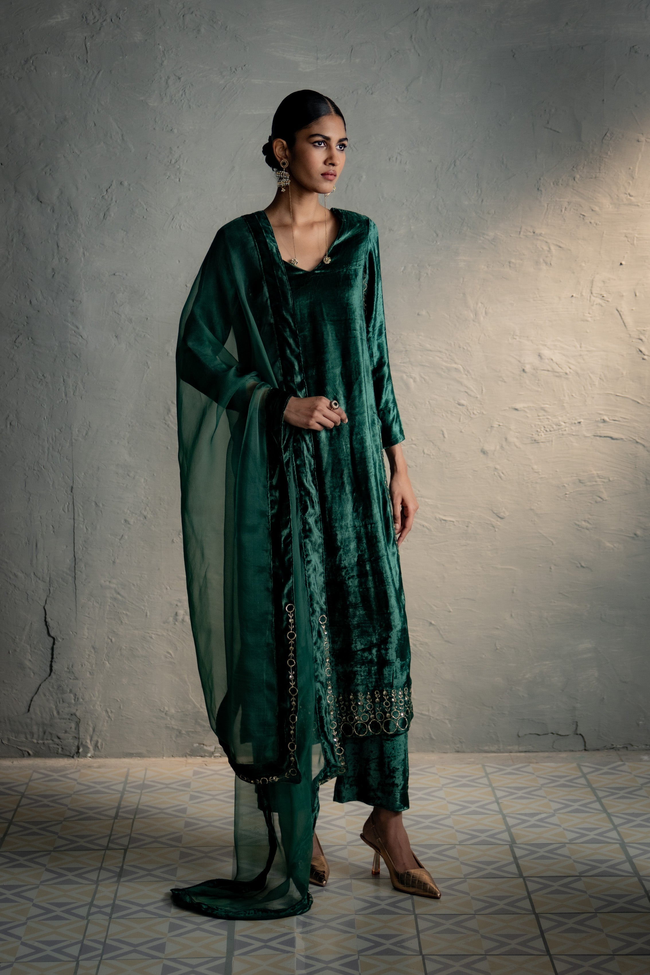 Woman wearing a green traditional outfit against a gray wall.